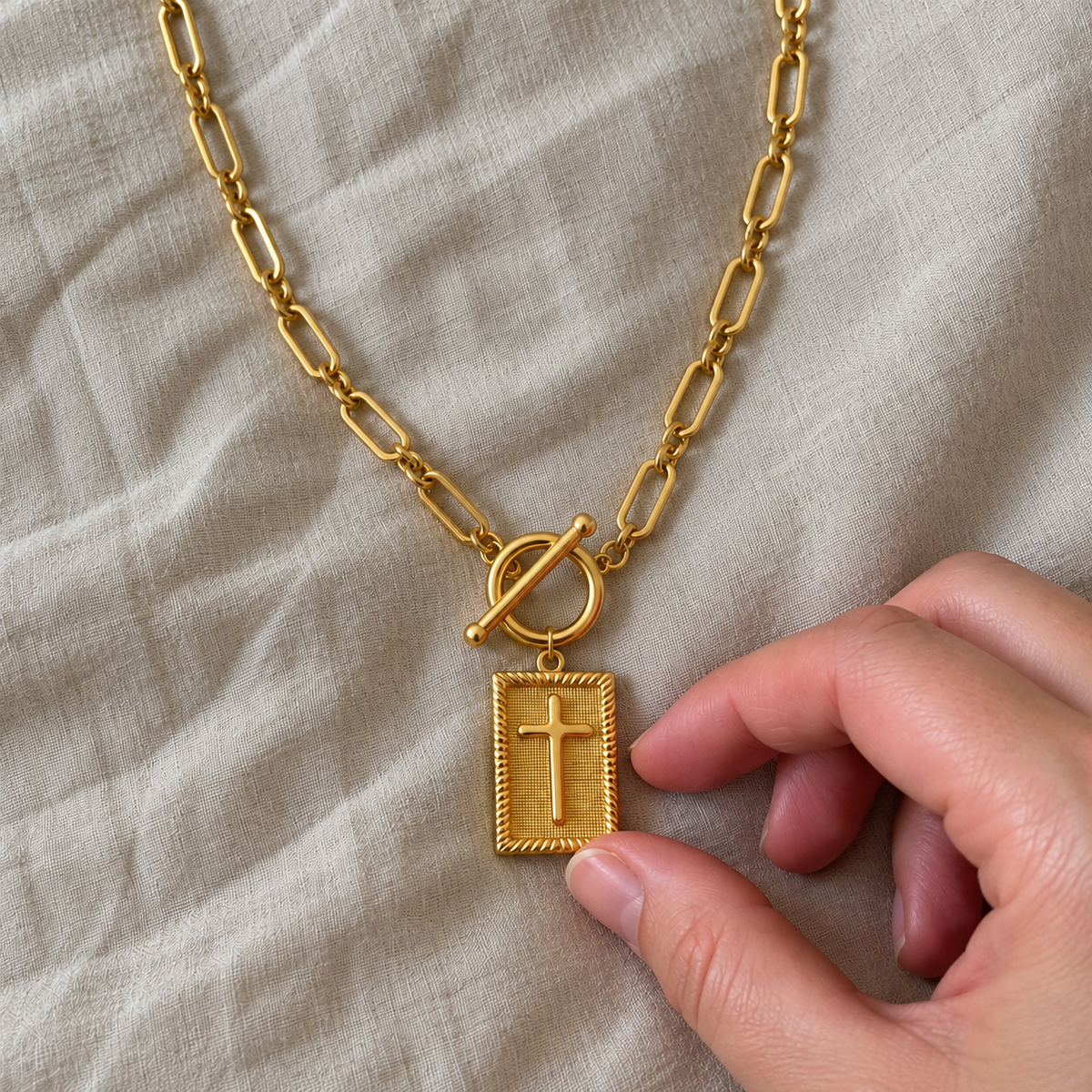 Dettaglio della Collana Croce Paperclip sul lino, mano sul ciondolo